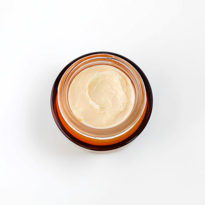 An open amber glass jar containing a light beige face cream , photographed from above on a plain white background.